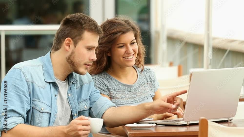 Happy couple talking about on line laptop content in a bar terrace Happy couple talking about on line laptop content in a bar terrace