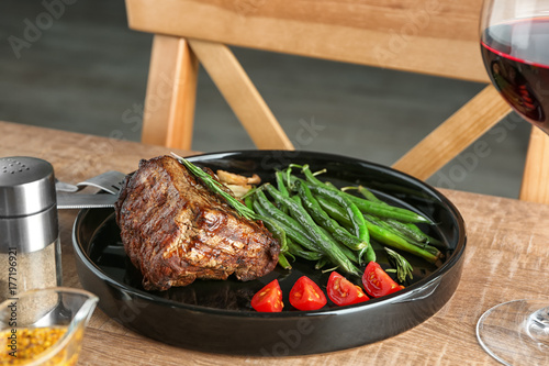 Plate with delicious grilled steak and vegetables on wooden table