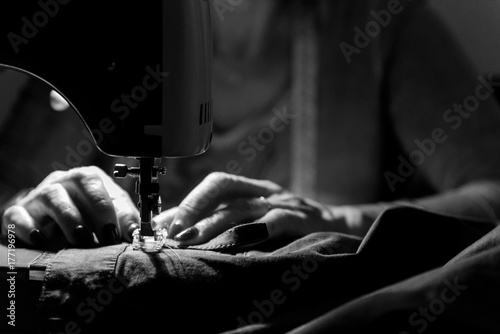 Close up on sewing machine and seamstress' hand while she is working. Black and white
