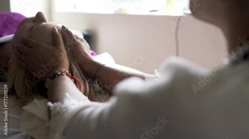 Very tight shot of a polarity therapists hands on her client’s head as the camera moves from right to left. Client is a mature caucasian woman.