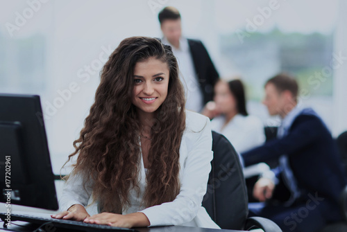 Happy young businesswoman looking behind and her colleagues work