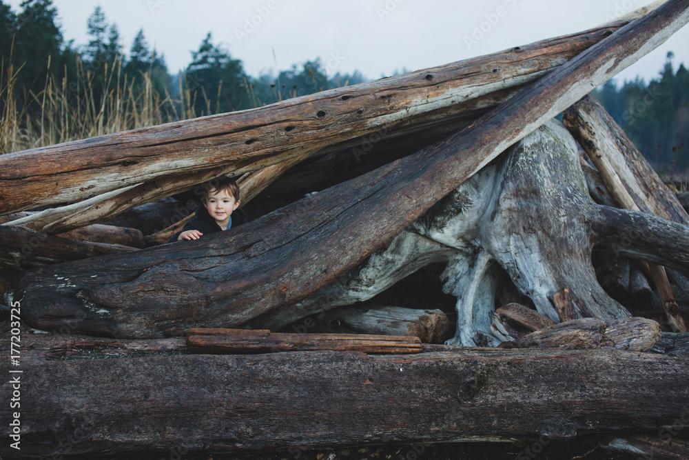Dapper toddler boy playing in log fort in winter Dapper toddler boy playing in log fort in winter