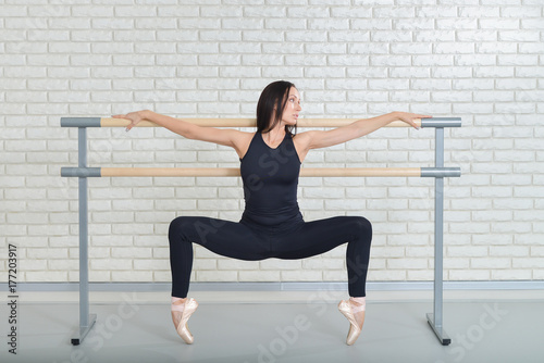 Beautiful ballet dancer practicing near barre at ballet studio, Ballerina full length portrait.