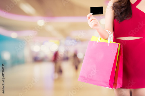 Portrait of asian woman wear red dress holding shopping bag and credit with smile and happy - Beautiful girl with buying with credit card on blur bokeh background - consumerism or payment concept.