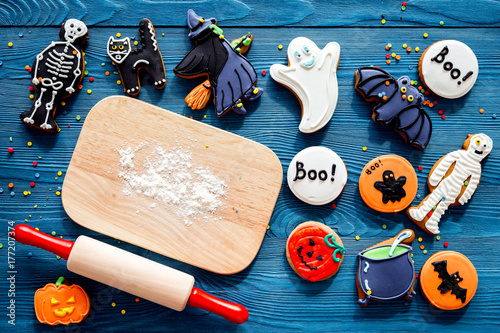Cook halloween gingerbread cookies in shape of skeleton, mummy. Sweets near desk and rolling pin. blue background top view copyspace