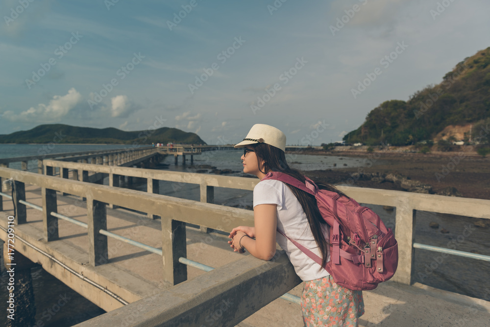 Portrait of young asian woman with backpack walking on the old sea pier at Rayong beach in Thailand. Have a vacation and travel concept.