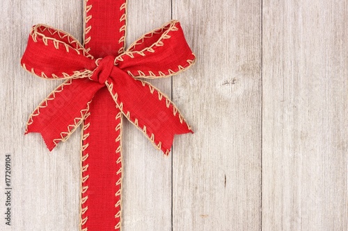 Rustic red Christmas bow and ribbon side border, above view on an old white wood background