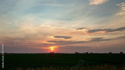 Gorgeous creamsicle orange sun setting in blue cloudy smokey sky in rural Idaho with silhouette of potato field photo