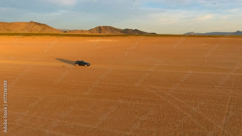 Aerial tracking shot of a car moving across a dry lake in the desert