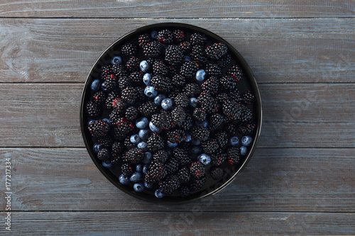 Plate with delicious ripe blackberries and blueberries on wooden background