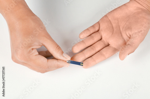 Woman using test strip for glucose level measurement on white background. Diabetes concept