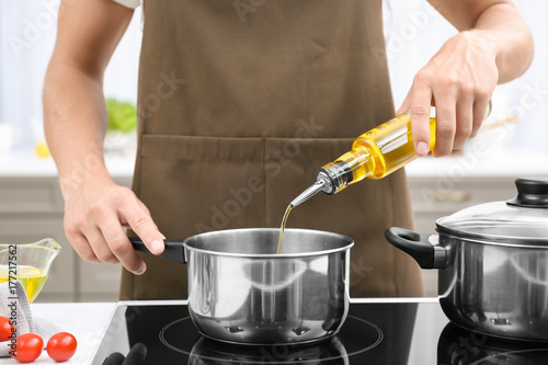 Man pouring cooking oil from bottle into saucepan on stove