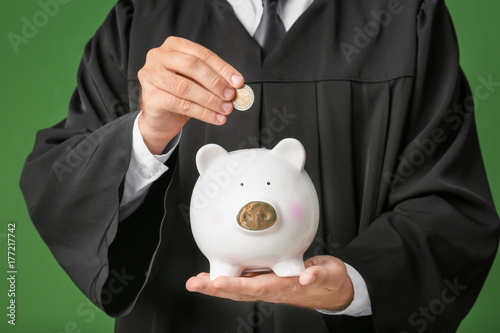 Young graduate putting coin into piggy bank, closeup