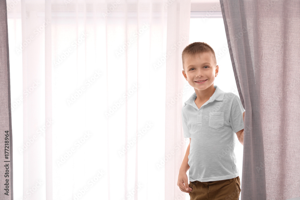 Cute boy standing near window with beautiful curtains indoors Cute boy standing near window with beautiful curtains indoors