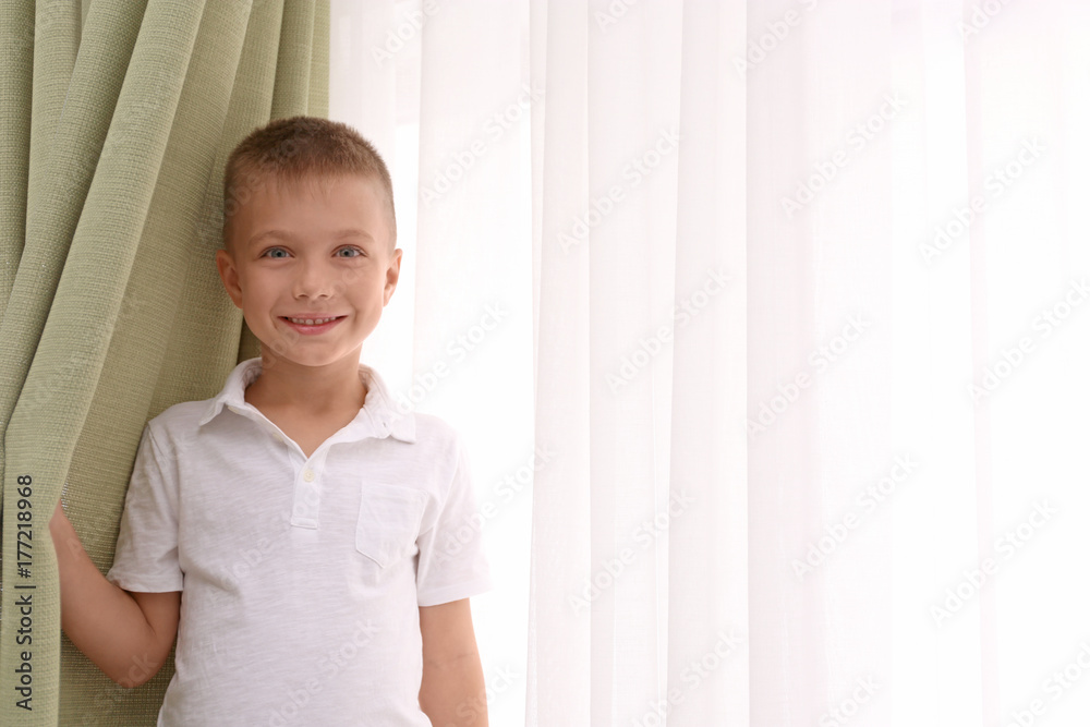 Cute boy standing near window with beautiful curtains indoors Cute boy standing near window with beautiful curtains indoors