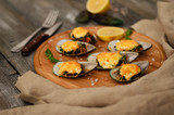 Mussels baked with spinach and Parmesan cheese with lemon and mint on a wooden desk