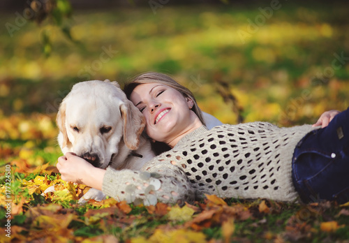 The blonde lies in yellow leaves with her labrador in the park in autumn photo