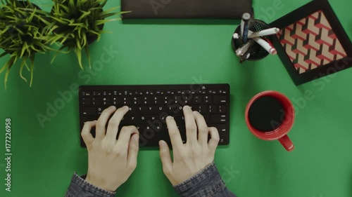 Top down shot of man typing on keyboard and taking a break to take a sip out of cup of coffee