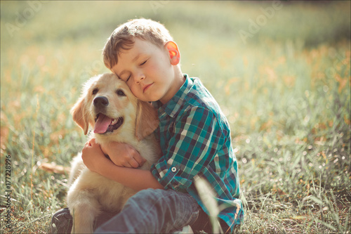 Cute handsome boy teen with blue eyes playing outdoor with amazing white pink labrador retriever puppy enjoying summer sunny day vacation weekend with full happyness.Happy smiling kid with best friend