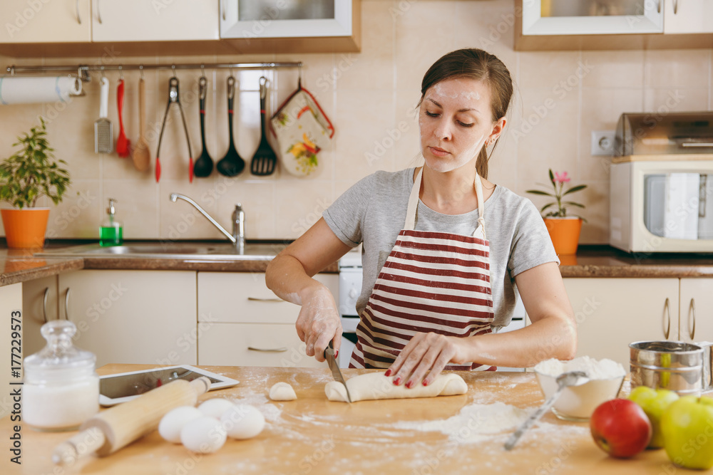A young beautiful happy woman sitting at a table, cuts a dough with a knife into pieces and going to prepare a Christmas cakes in the kitchen. Cooking home. Prepare food. A young beautiful happy woman sitting at a table, cuts a dough with a knife into pieces and going to prepare a Christmas cakes in the kitchen. Cooking home. Prepare food.