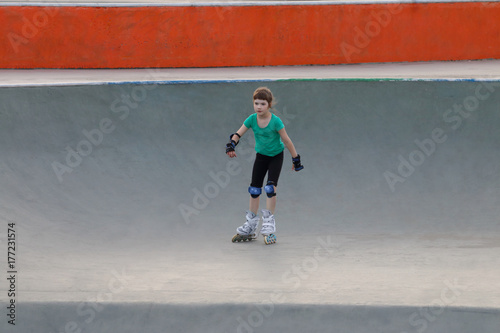 Happy girl roller skates on sport playground with ramps at summer day