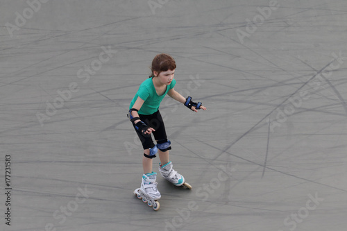 Girl child roller skates on sport playground with ramps at summer day