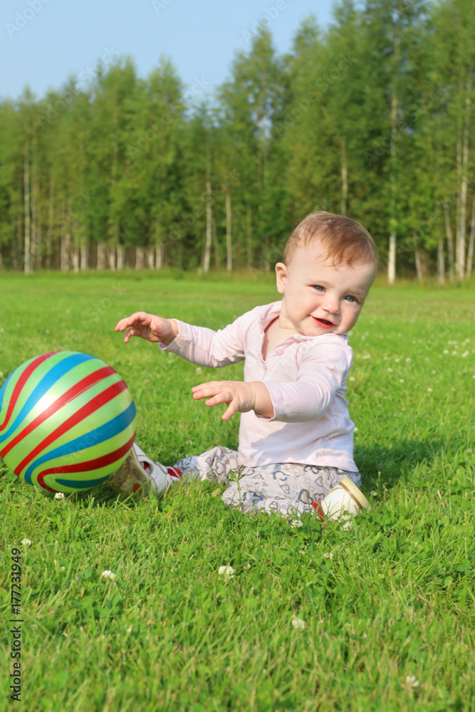 Cute smiling baby with ball sits on green grass on summer field Cute smiling baby with ball sits on green grass on summer field