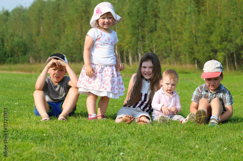 Five happy children sit and stand on green grass on summer field