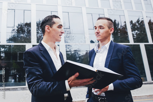 Two businessman with a notebook standing on the street in the background of the modern city