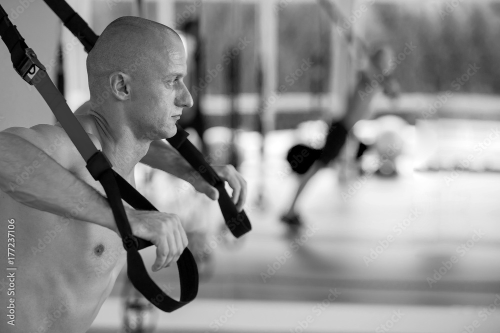 Beautiful young sports people are working out with TRX in gym foto de