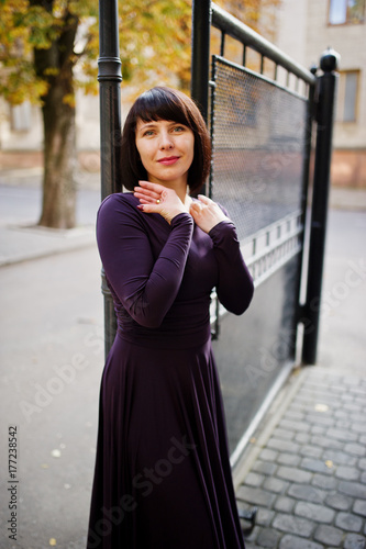Adult brunette woman at violet gown background black iron gates.