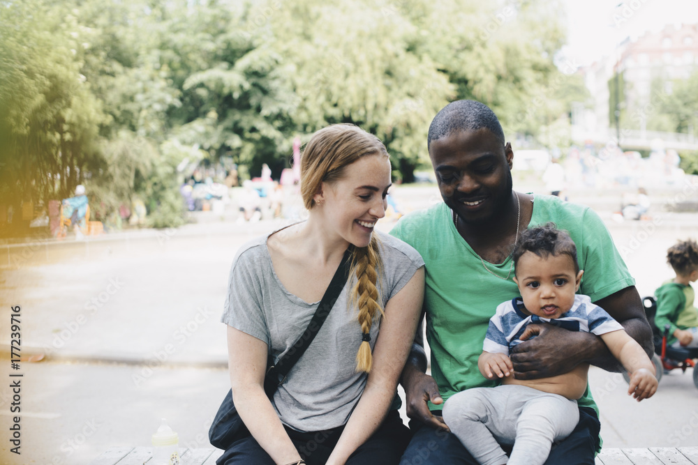 Smiling parents sitting with toddler at park