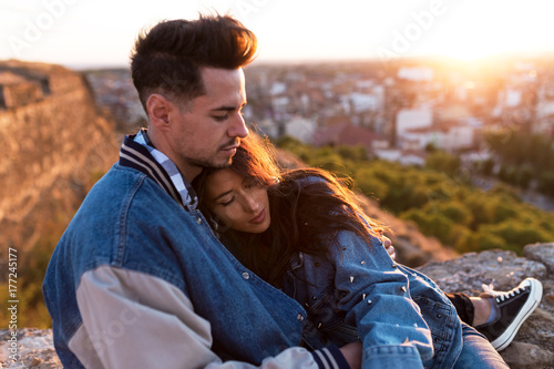 Beautiful young couple in love standing at a building rooftop at the sunset.