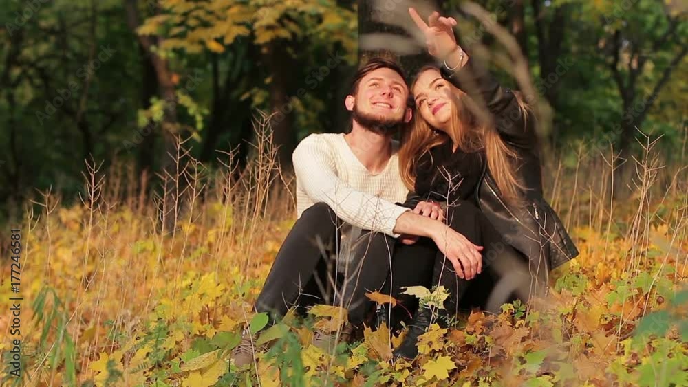 Couple sitting under a tree in an autumn forest or park. They are ...