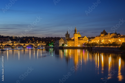 Lit Charles Bridge (Karluv most), Old Town and their reflections on the Vltava River in Prague, Czech Republic, at dusk. Copy space.