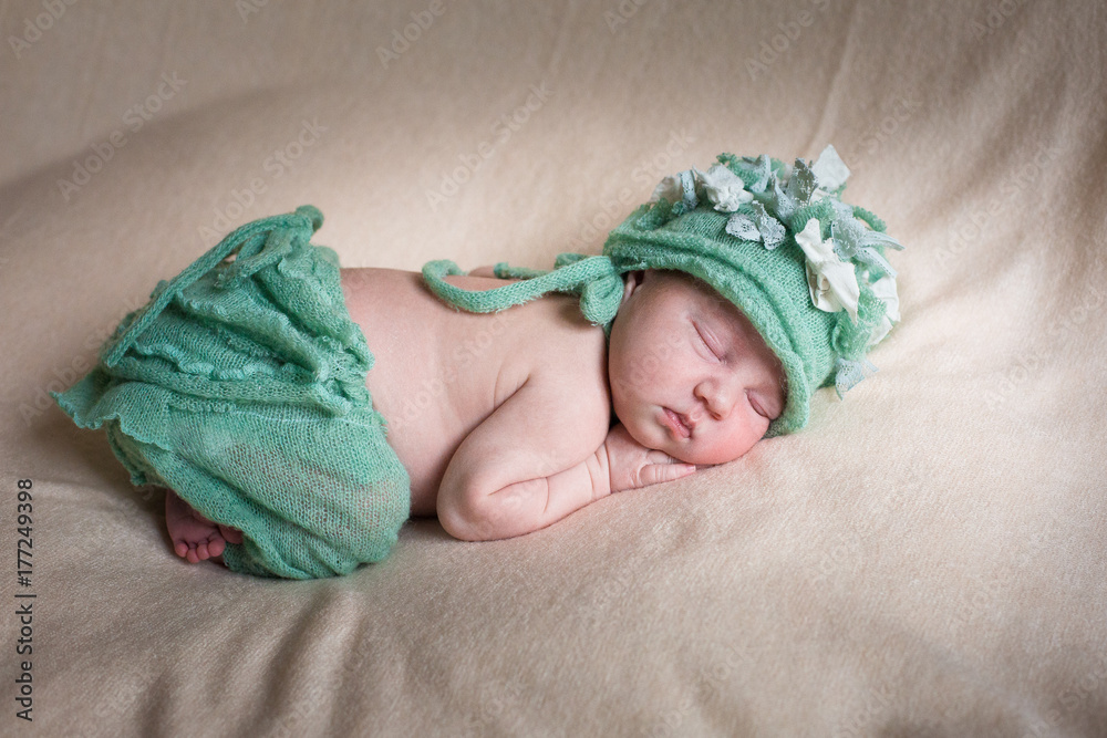 Sleeping newborn baby girl in a green knit panties and hat. Sleeping on a covered sheet. Sleeping newborn baby girl in a green knit panties and hat. Sleeping on a covered sheet.