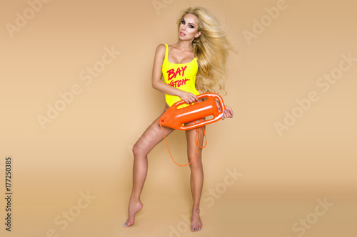 Sexy lifeguard with long blonde hair, standing in bikini with rescue board