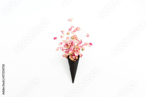 Black ice cream waffle cone with dry pink roses petals isolated on white background. Flat lay  top view flower concept.