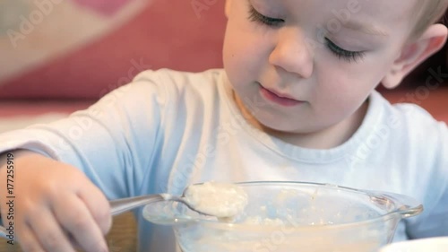 A cute little boy eats porridge with pieces of meat at a children's table. home furnishings