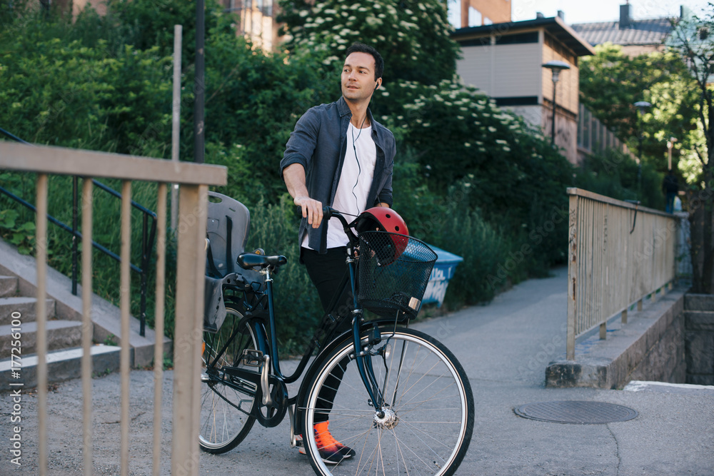 Mid adult man walking with bicycle on footpath in city Mid adult man walking with bicycle on footpath in city