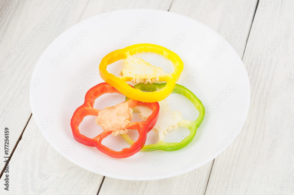 Three slices of colored red and green and yellow fresh ripe raw pepper in ceramic bowl on old rural white wooden planks Three slices of colored red and green and yellow fresh ripe raw pepper in ceramic bowl on old rural white wooden planks