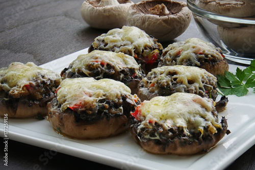 Stuffed mushrooms with cheese, bacon and vegetables on white serving plate