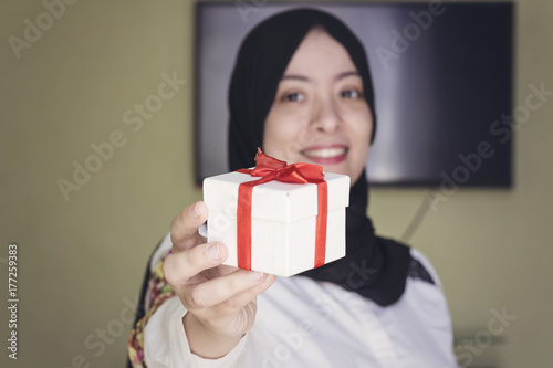 beautiful muslim woman with cheerful smile give you white gift box with red ribbon