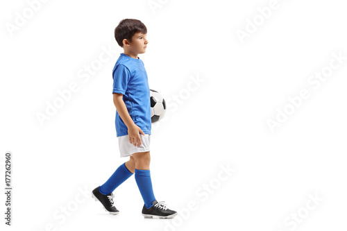 Little soccer player holding a football and walking