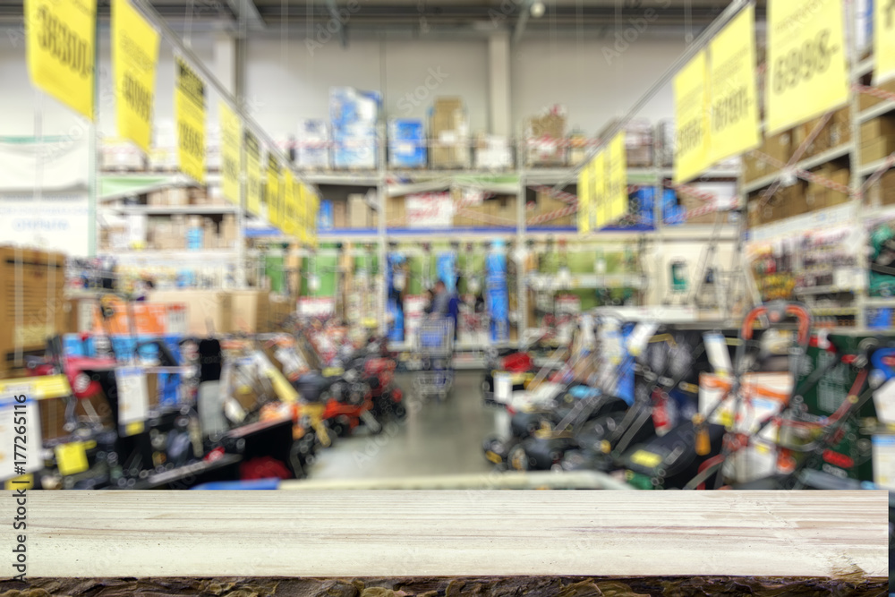Fototapeta premium Shop of garden machinery and equipment. Lawn mowers. Defocused image. Wooden table top or counter in the foreground.