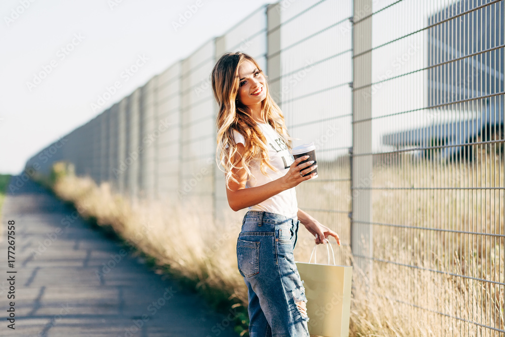 Beautiful woman walking with coffee and shopping bag in white T-shirt with word 