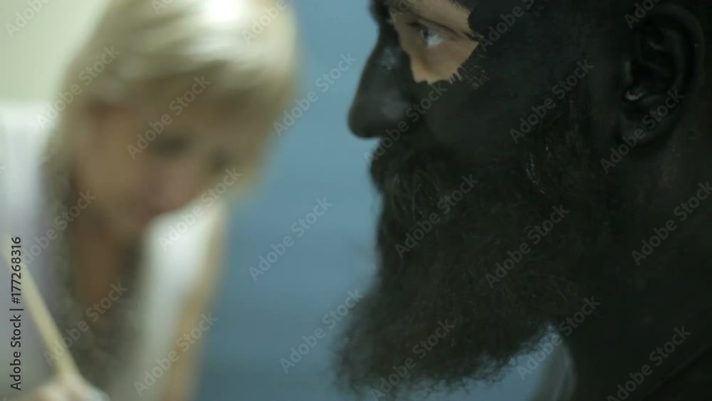 Makeup with black ink for shooting of a bearded man. Backstage
