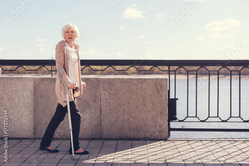 Fotografering Elderly woman walking along the bridge on crutches