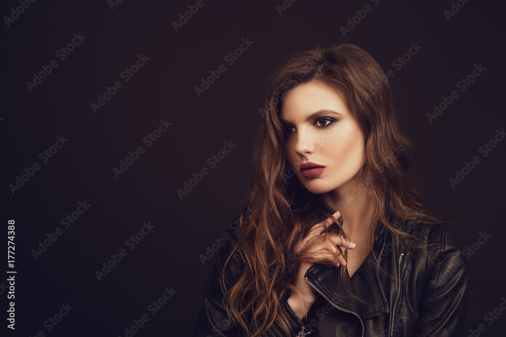 Portrait of the beautiful young woman with wavy brown hair posing at studio over black background. Toned.