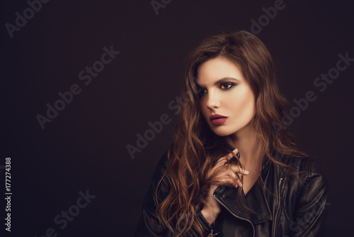 Portrait of the beautiful young woman with wavy brown hair posing at studio over black background. Toned.